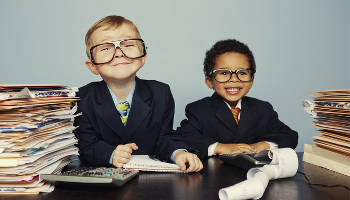 two young kids dressed in business suits at a desk with papers