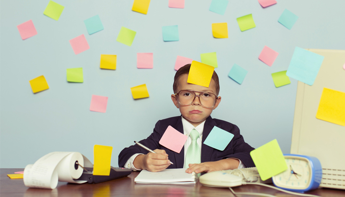 young kid in business suit sitting at desk covered in sticky notes